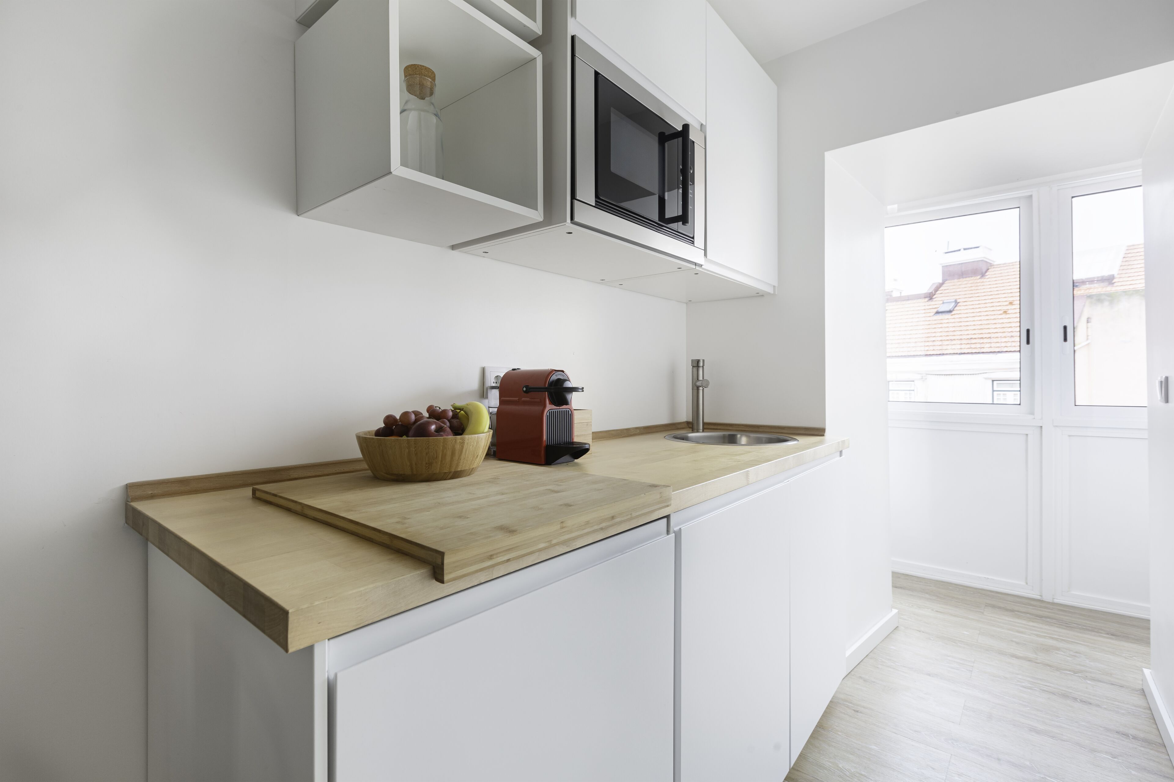 A modern kitchen with white cabinets, a wooden countertop, a built-in microwave, and a sink.