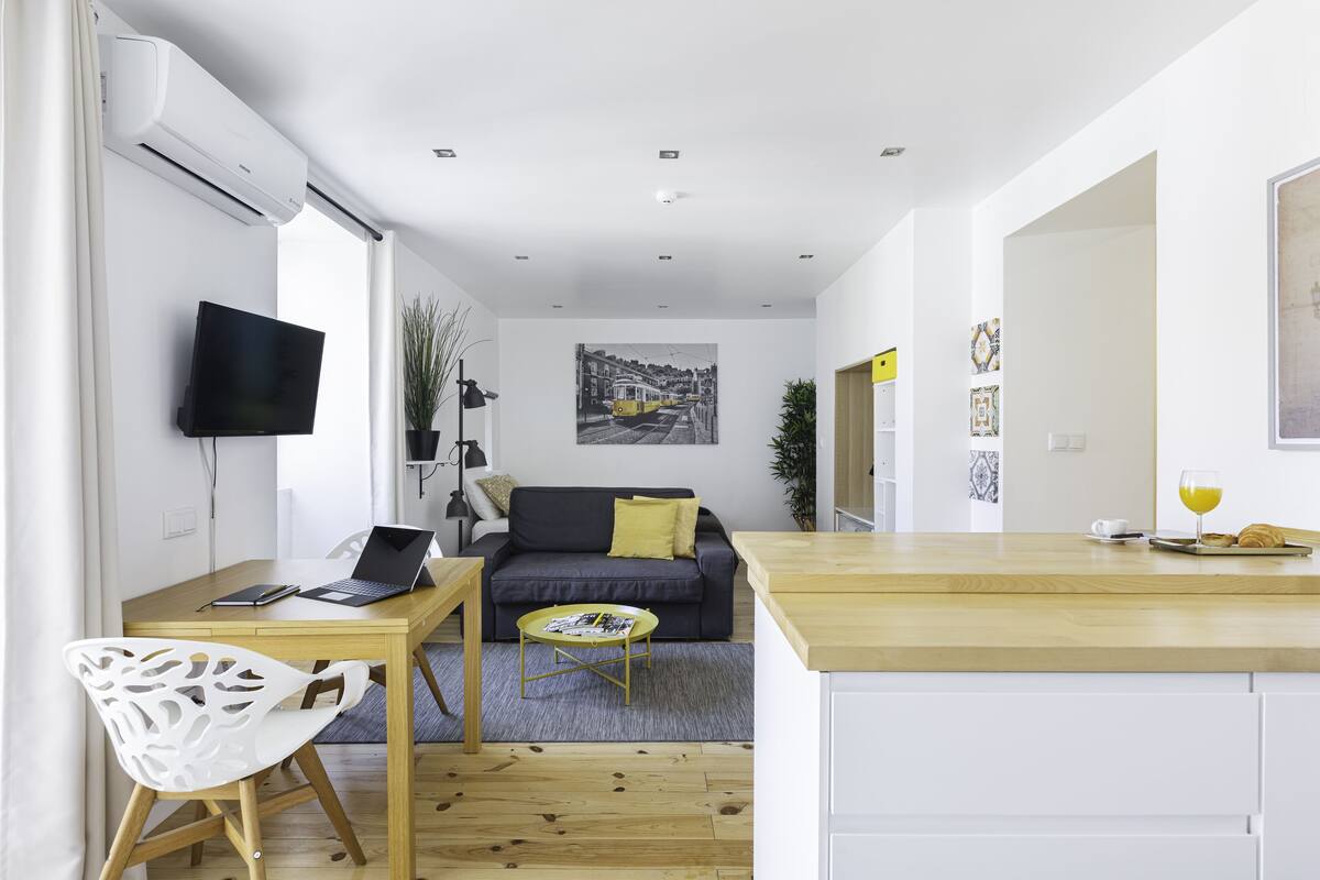A modern living space with a dining area, a sofa, a TV, and a kitchen counter.