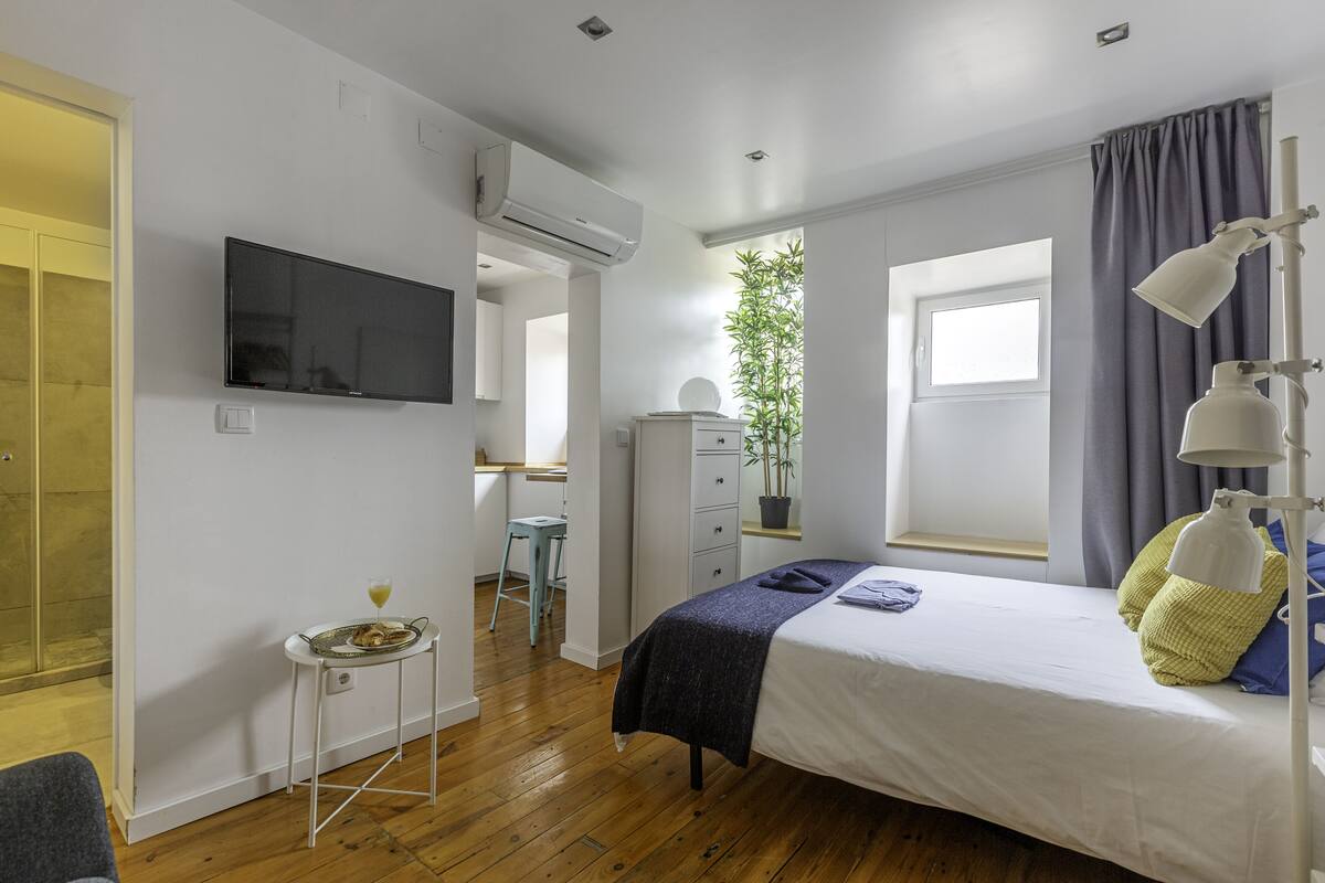 A bedroom with a bed, a desk, a chair, a television, and a window.