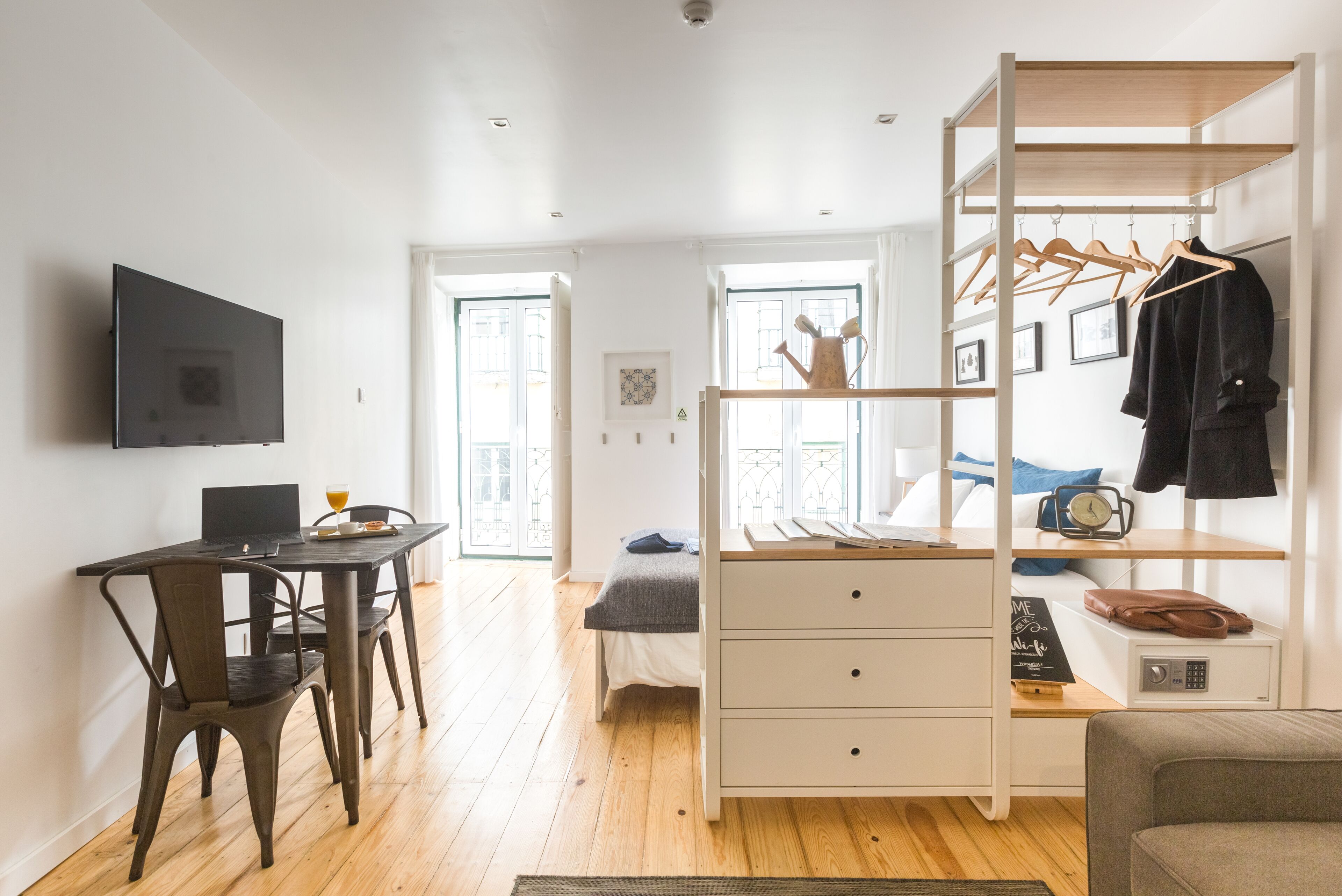 Ein modernes Schlafzimmer mit Bett, Schreibtisch mit Laptop, Kleiderschrank und Fernseher an der Wand.