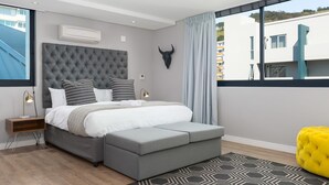 A modern bedroom with a tufted headboard, a large window with curtains, a bull's head wall decoration, and a bright yellow ottoman. - Warwick 401 - Adults Only (Cape Town)