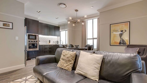 Una sala de estar moderna con un sofá de cuero, un comedor con mesa y sillas, y una cocina con armarios oscuros y electrodomésticos integrados.