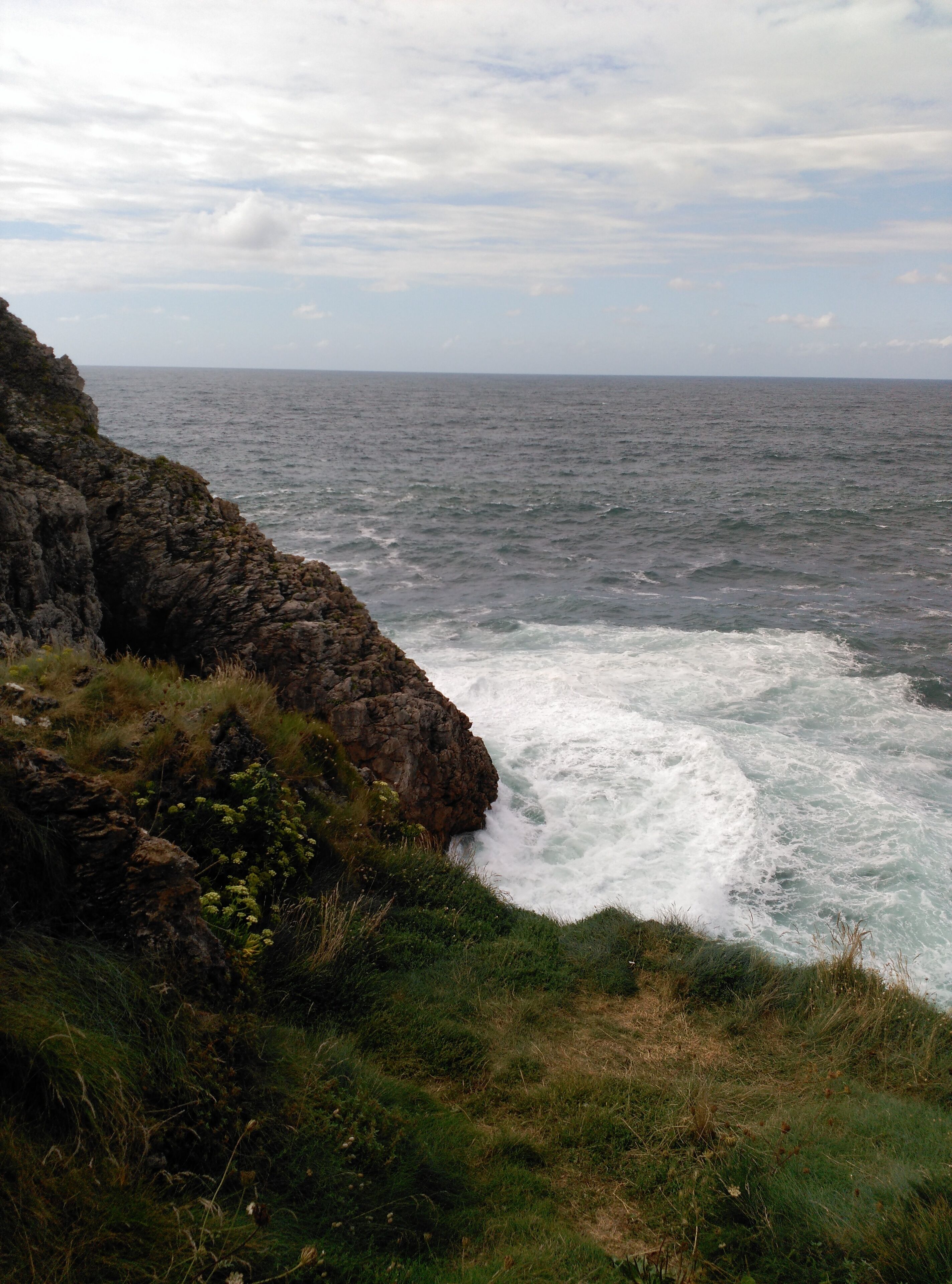 A coastal landscape with rocky cliffs and waves crashing against the shore.