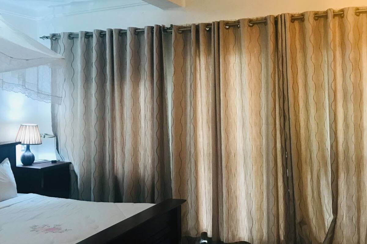 Una habitación de hotel con cama, mesita de noche con lámpara y ventana con cortinas.