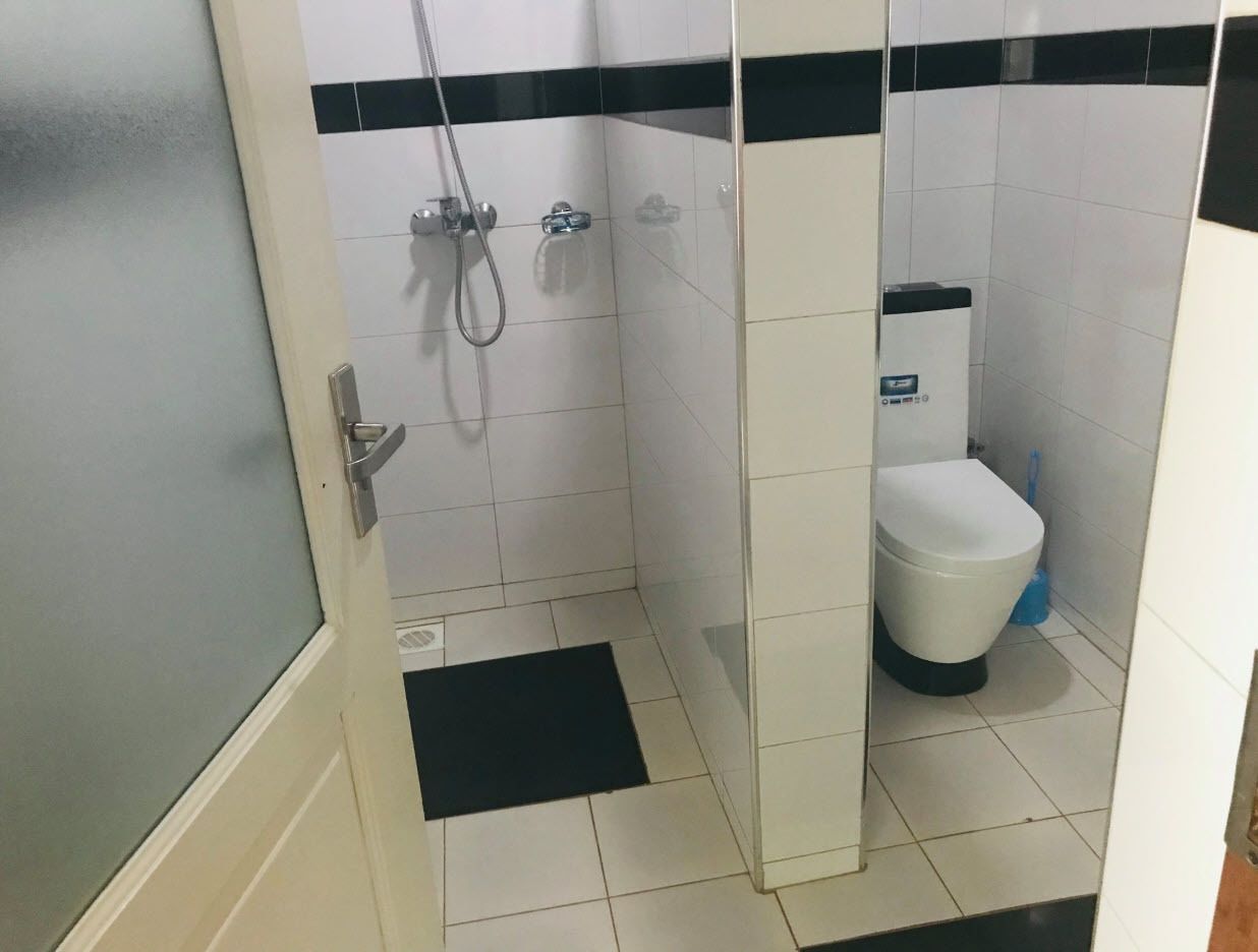 A small, enclosed bathroom with a toilet, a shower, and a black mat on the floor.