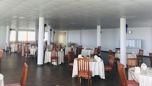 A spacious dining hall with multiple tables and chairs, white ceiling, and large windows.
