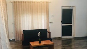 A room with a black armchair, a wooden side table with a plant, a patterned curtain, and a door with a screen.