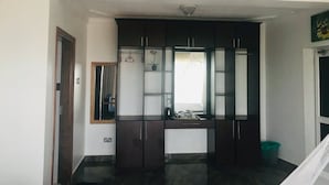A room with a dark wooden wardrobe, a small window with curtains, and a mirror on the wall.