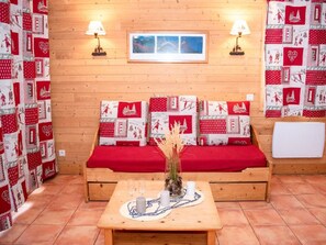 A cozy room with a wooden sofa, two wall-mounted lamps, a framed picture, and a small table with a vase and candles.