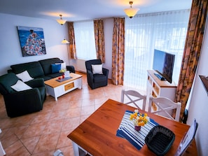 A living room with a sofa, armchair, coffee table, TV, and a painting on the wall. - 3 Room A 13 - Wohnpark Binz (with indoor pool) (Binz)