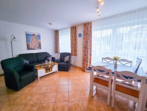 Un salon comprenant un canapé, un fauteuil, une table à manger et des chaises. Il y a un tableau au mur et une horloge.