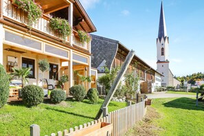 Un edificio europeo tradicional con un balcón, una torre de iglesia y un jardín bien cuidado.