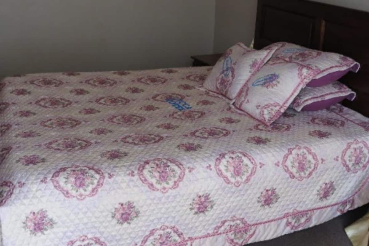 A neatly made bed with a patterned bedspread and pillows, a wooden nightstand, and a dark-colored dresser.