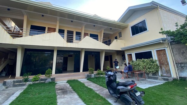 A two-story building with a covered patio area, a staircase, and a parked scooter. - Laguno Bed and Breakfast (Moalboal)