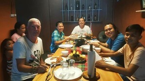 A group of people seated around a wooden table with plates of food, glasses, and a bottle. - Laguno Bed and Breakfast (Moalboal)