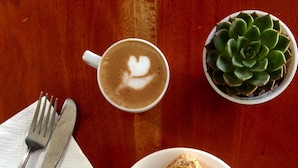 A table with a plate of toast topped with banana slices, a cup of coffee with latte art, a succulent plant, and cutlery on a napkin. - Laguno Bed and Breakfast (Moalboal)