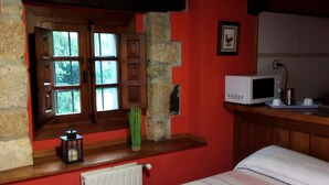 Un dormitorio con cama, ventana, pared de piedra, banco de madera, radiador y microondas.