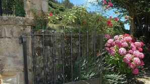 Un muro de piedra con una verja de metal, un jardín de rosas rosadas y un edificio de piedra al fondo.