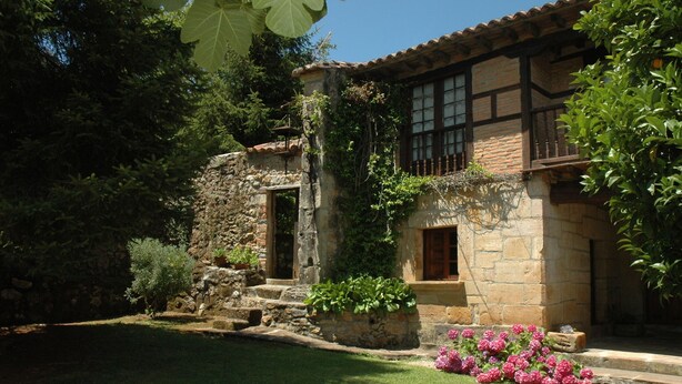 Un edificio de piedra con tejado de tejas, una escalera de piedra y un jardín con flores rosas.