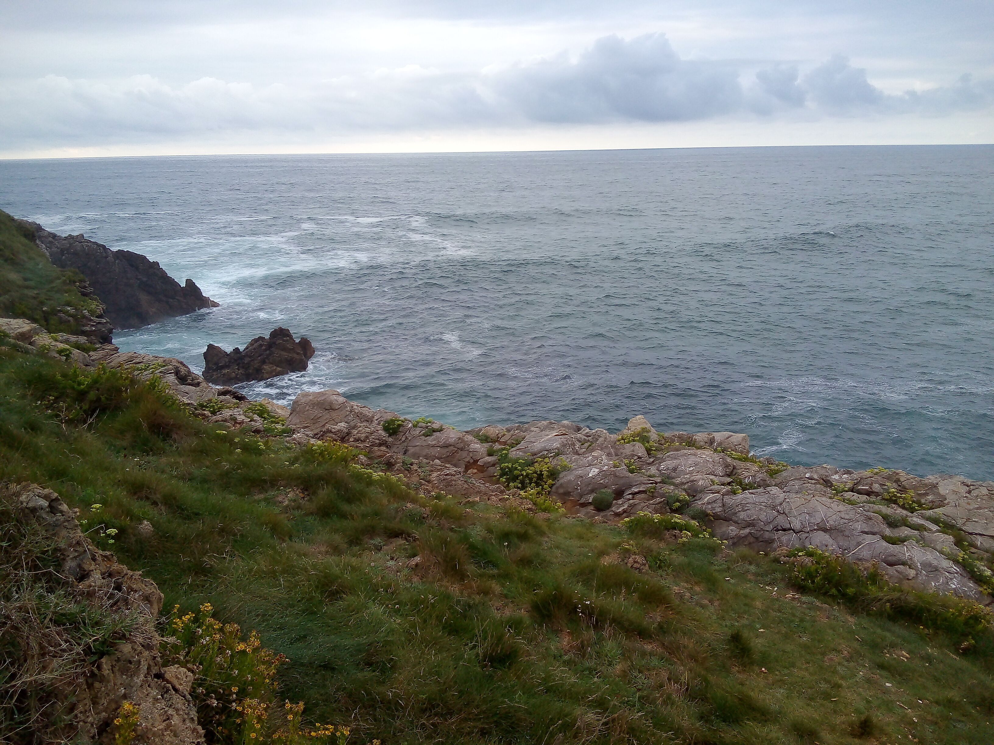 Un paysage côtier caractérisé par un terrain rocheux et des zones herbeuses.