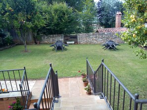 Un jardin avec un mur en pierre, une cheminée en briques et un espace patio aménagé avec du mobilier d’extérieur.