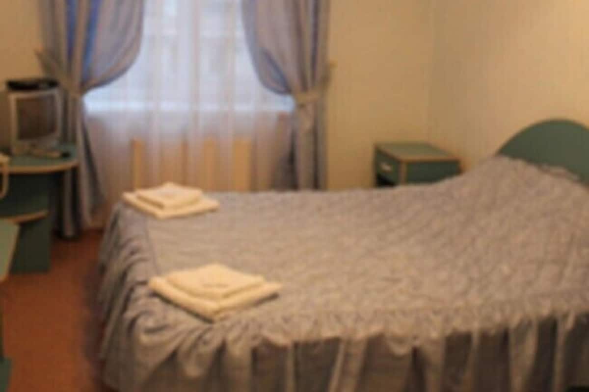 A bedroom with a bed, a nightstand, a television, and a window with curtains.