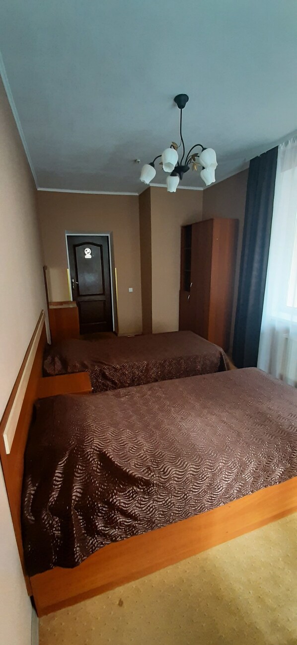 Una habitación con dos camas, un armario, una puerta y una lámpara en el techo.