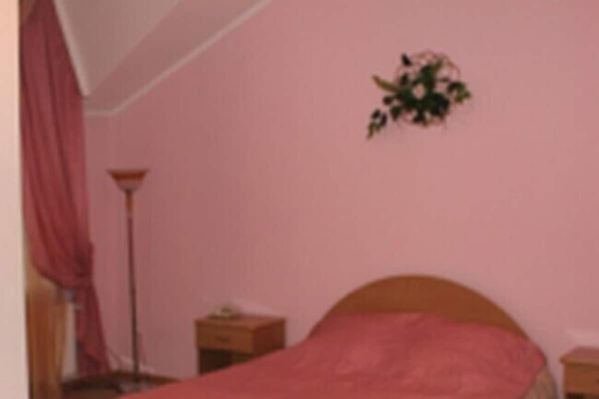 A bedroom with a single bed, a nightstand, a lamp, and a wall-mounted flower arrangement.