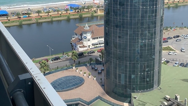A high-rise building with a glass facade overlooking a coastal area with a beach and water body. - Orbi city Davide (Batumi)