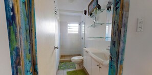 Une salle de bain comprenant des toilettes, un lavabo et une douche. Une fenêtre permet à la lumière naturelle d’entrer.