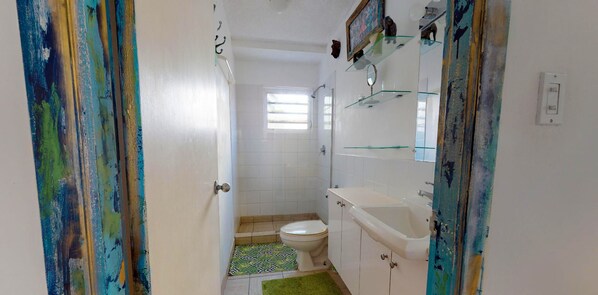 Baño con inodoro, lavamanos y ducha. Cuenta con una ventana que proporciona luz natural.