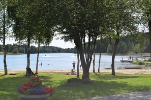 Un parque junto al lago con un embarcadero, árboles y un césped lleno de flores.
