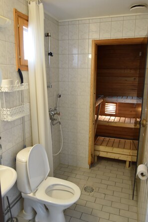 Un baño con inodoro, ducha y sauna de madera.