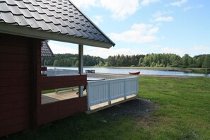 Une cabane en bois dotée d’une terrasse donnant sur un lac, entourée d’une forêt.