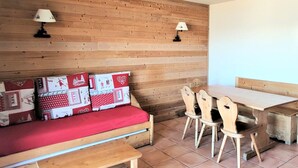 A cozy room with a wooden wall, a red sofa with patterned cushions, a wooden table, and two chairs. - 3-room apartment, sleeps 8, balcony, parking (Uvernet-Fours)