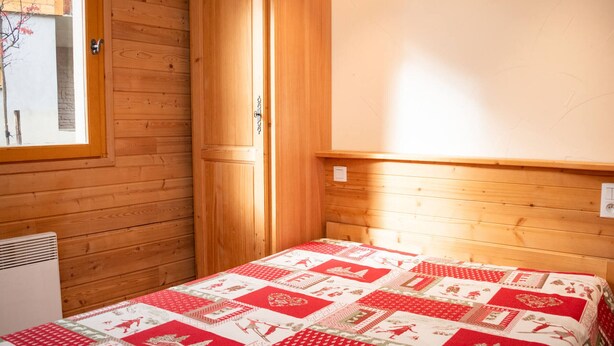 A wooden room with a bed, a window, and a wall-mounted heater. - 3-room apartment, sleeps 8, balcony, parking (Uvernet-Fours)