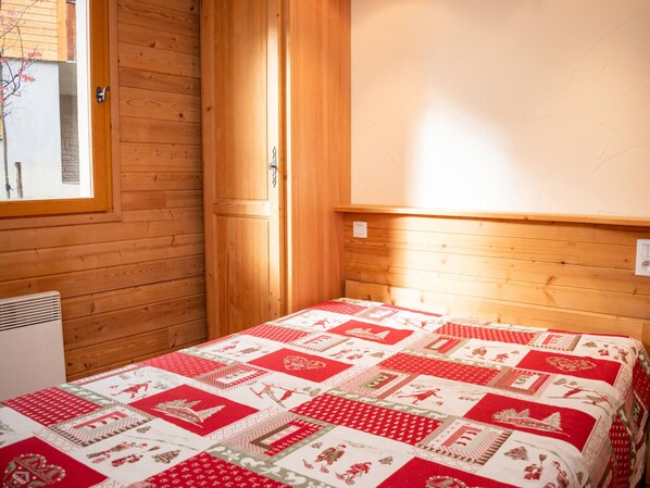 Une pièce en bois avec un lit, une fenêtre et un radiateur fixé au mur.