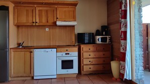 A compact kitchen with wooden cabinets, a dishwasher, an oven, a microwave, and a coffee maker. - 3-room apartment, sleeps 8, balcony, parking (Uvernet-Fours)