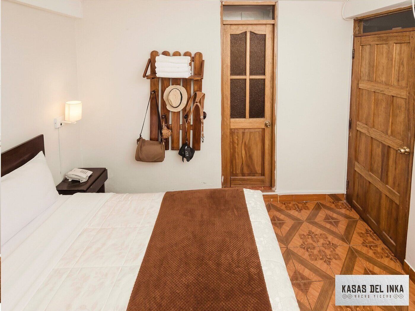 Een hotelkamer met een bed, nachtkastje, een handdoekrek aan de muur, een deur en een vloer met patroon.
