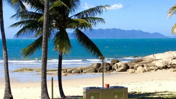 A beach with palm trees, a rocky shoreline, and a clear view of the ocean. - Golden Sands Beach House, Rose Bay,  Bowen (Bowen)