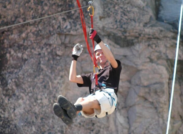 A person engaged in an outdoor activity, suspended by a harness and ropes, with a rocky background.