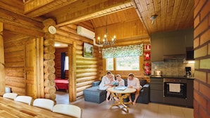 A log cabin interior with a dining area, a kitchen, and a seating area with a chandelier. - Serena Villas (Espoo)