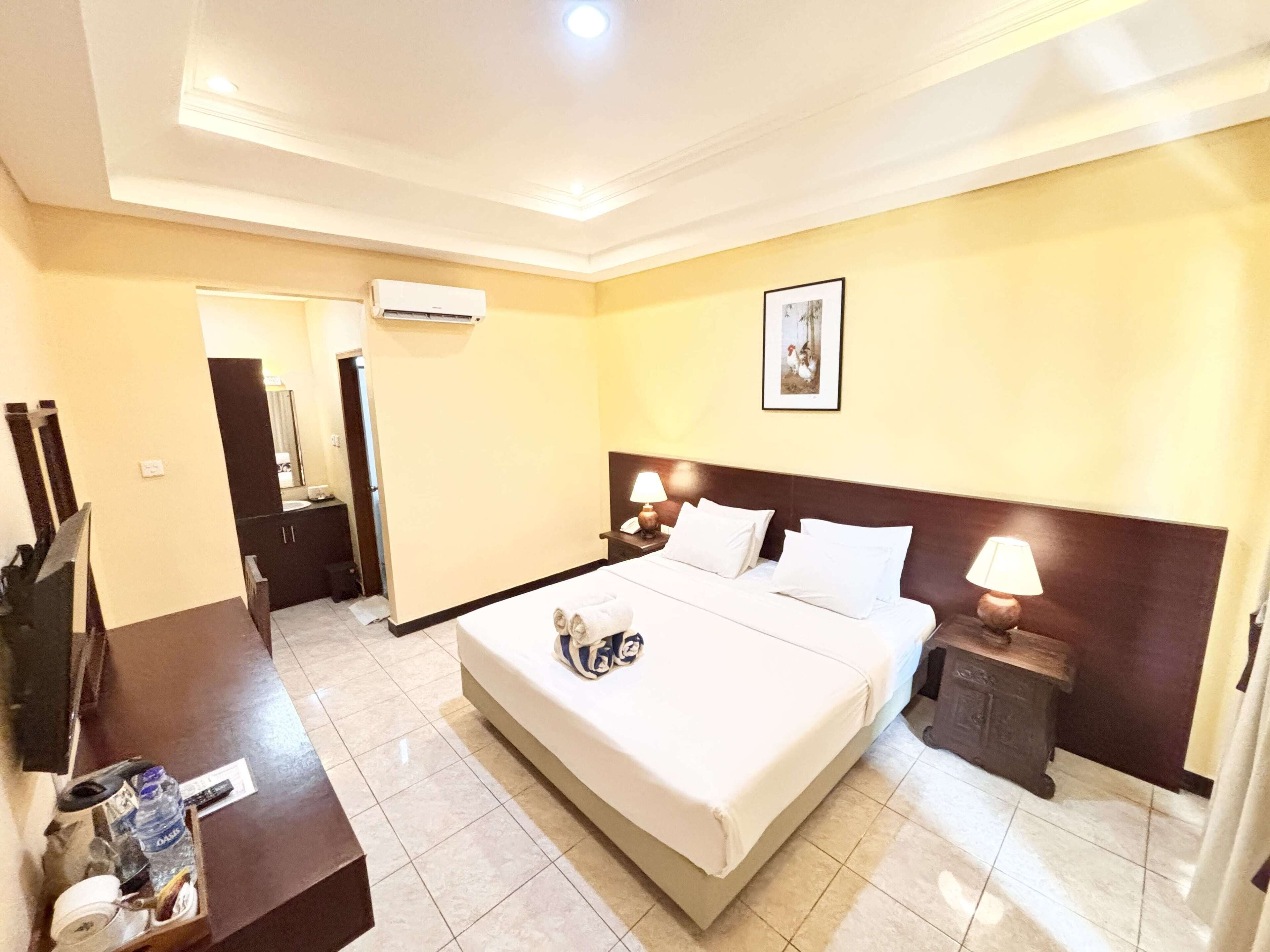 A hotel room with a large bed, bedside lamps, a small table, and a wall-mounted air conditioner.