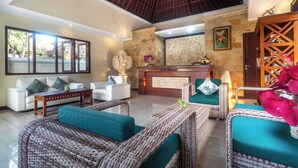 A spacious living area with wicker furniture, a stone fireplace, and a large window overlooking greenery. - Hotel Segara Agung (Denpasar)