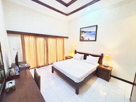 A hotel room with a large bed, two bedside tables with lamps, a flat-screen TV, a window with curtains, and a painting on the wall.