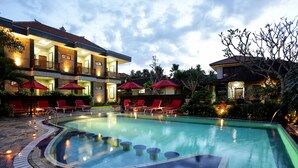 A hotel with a swimming pool, red umbrellas, and lounge chairs. - Hotel Segara Agung (Denpasar)