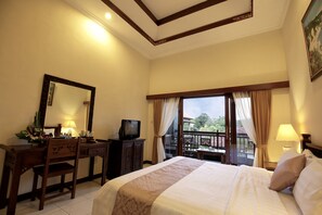 A hotel room with a bed, a desk, a television, and a balcony with curtains.