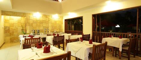 Un restaurante con varias mesas, cada una con mantel blanco y servilleta roja.