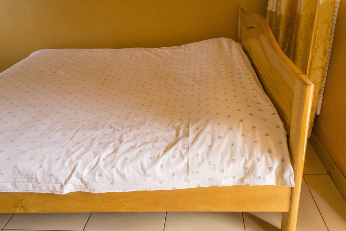 A single bed with a wooden frame and a white mattress with a subtle pattern.