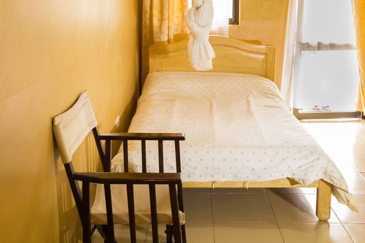 A room with a bed, a chair, a window with curtains, and a mosquito net.
